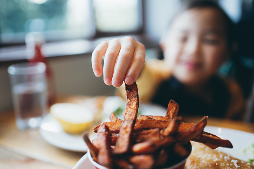 Asian little girl reaching for sweet potato fries in a restaurant.