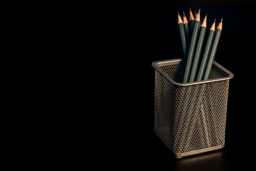 Simple pencils in an iron stand on a black background