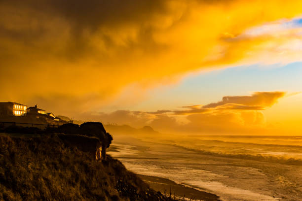 A clean white golden sun peaks over the horizon and the early morning sunlight reflects in the waves of the Pacific Ocean. Silhouetted palm trees decorate the cliffs of Malibu's La Piedra State Beach.The photo is taken from high on the cliffs looking down on the beach. There are no clouds in the sky, and no people on the beach.