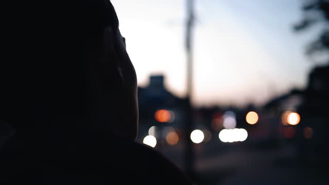 A teenager walks through the evening city against the background of city lights and passing cars. Shooting from behind in motion