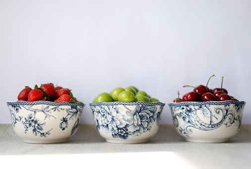 Istanbul, Turkey-May 20, 2021: Fresh strawberries, cherries and sour green plums on three porcelain plates in front of a gray concrete floor and a white background. The plates are porcelain plates with blue floral patterns. Shot with Canon EOS R5.
