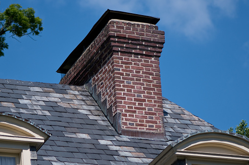 Closeup of attic windows and brick chimneys on house roof top covered with ceramic shingles. Tiled covering of building.