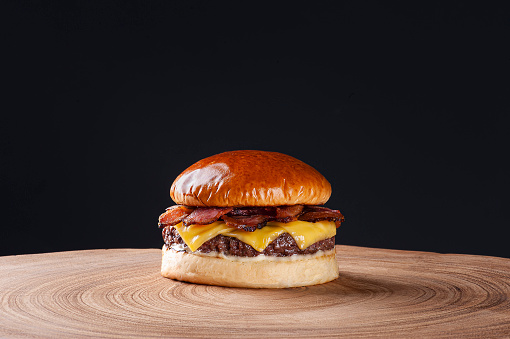 Delicious beef burger with bacon and cheddar cheese on wooden table on dark background. Copy space