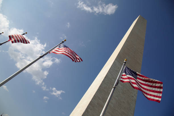 istock Three American flags in front of Washington Monument against blue sky with clouds. 1319685943