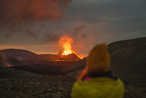 Person enjoying a magnificent view of a volcanic eruption in Iceland. Glowing volcano spewing fire from its volcanic crater. Powerful Mother Nature