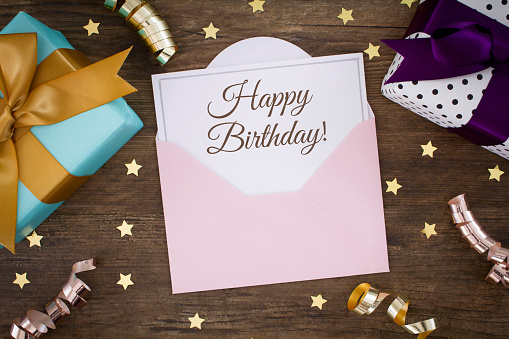 Happy Birthday written on a blank card with gift boxes, gold stars and ribbons. 
Shot from above on a wooden background.
Stock photo.