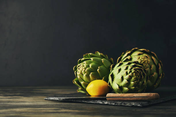 Still Life Background with Three Artichokes, Lemon and Kitchen Knife on a Slate Cutting Board