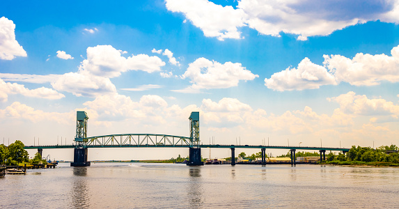 The Cape Fear Memorial Bridge, an iconic arch bridge crossing the Cape Fear River in Wilmington, NC, during a partly cloudy day.