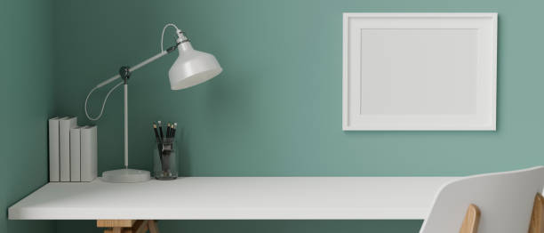 istock Stylish working space with stationery, books and lamp on white table and frame decorated on turquoise wall, 3D rendering 1319710775