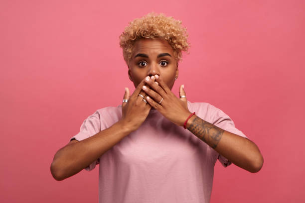 istock Dark-skinned woman with a frightened expression closes her mouth with her hands. 1319714469