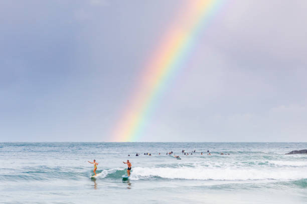 ein paar surft in der tea tree bay im noosa national park unter einem regenbogen, noosa heads. - coastline noosa heads australia landscape stock-fotos und bilder