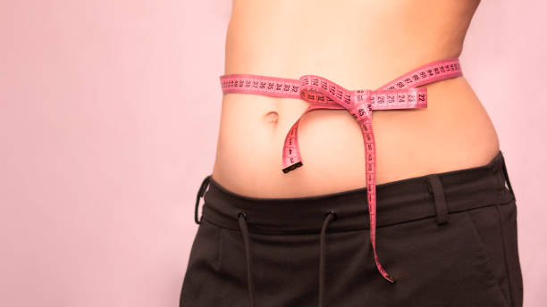 bow of centimeter ribbon on the waist of a woman, the concept of weight loss, healthy lifestyle. bow of centimeter ribbon on the waist of a woman, the concept of weight loss, healthy lifestyle. layout with copy space. stomach knot stock pictures, royalty-free photos & images