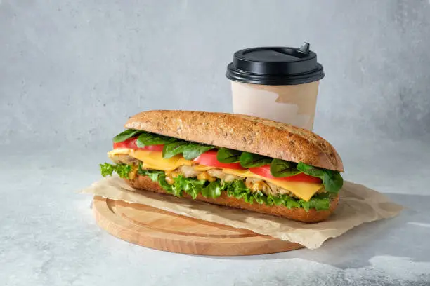 Sandwich with lettuce, tomatoes, chicken, cheese, sorrel and a cup of coffee (tea) on wooden cutting board.