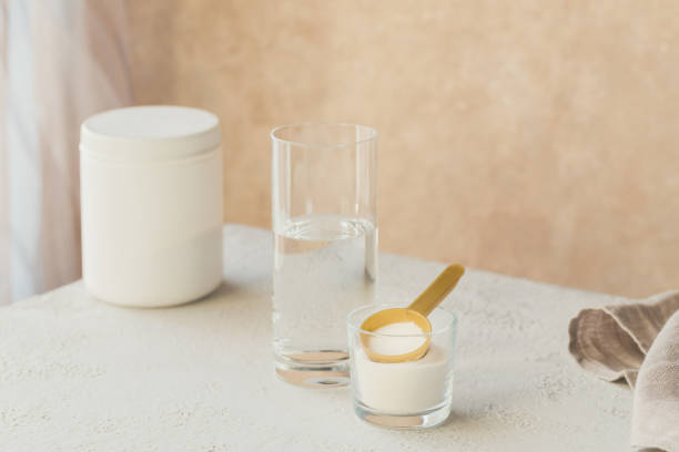 Collagen powder in bowl, glass of water and measure spoon on a white wooden background. Extra protein intake. Natural beauty and health supplement concept. Collagen powder in bowl, glass of water and measure spoon on white wooden background. Extra protein intake. Natural beauty and health supplement concept. human collagen stock pictures, royalty-free photos & images