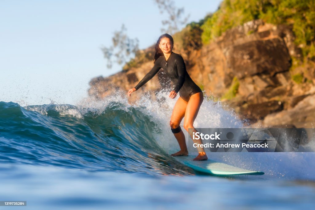 A woman is surfing a wave at Noosa National Park. A young woman is surfing a blue longboard on a wave at Tea Tree Bay in Noosa National Park. Noosa Heads Stock Photo