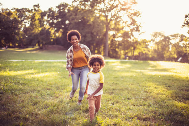 african american mother and daughter running trough park. focus on little girl. - family child portrait little girls imagens e fotografias de stock