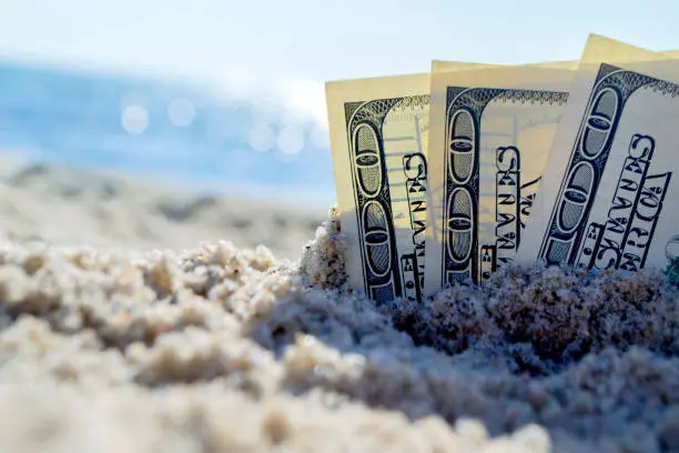 Three dollar bills are buried in sand on sandy beach near sea on sunny bright summer day close-up. Money grows in sand. Dollars buried in ground. Growing money in sand. One hundred dollar bill money.