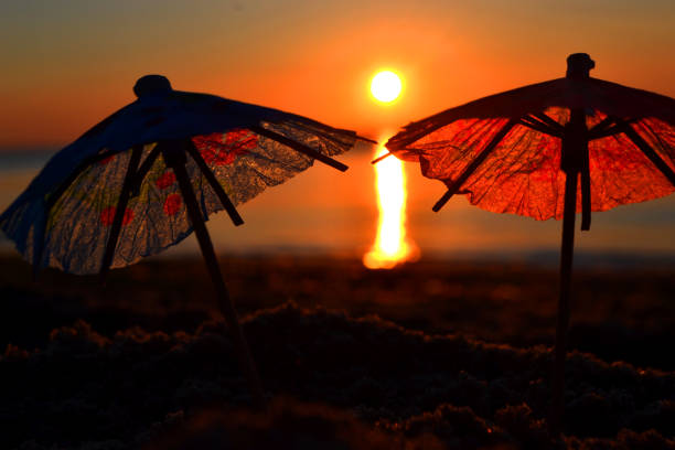 ombrelli da cocktail di carta nella sabbia sulla riva del mare all'alba del tramonto da vicino. - umbrella two objects cocktail drink foto e immagini stock