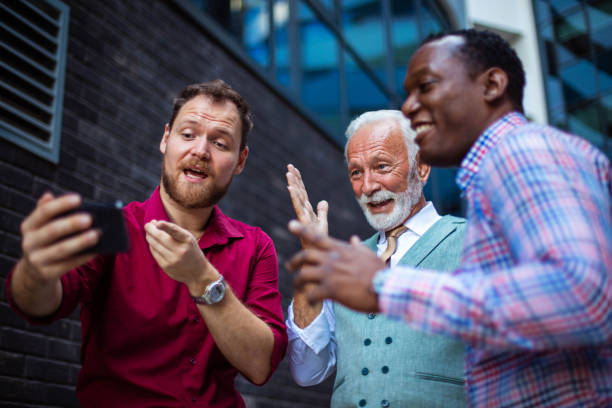 istock Three business men standing outside and using mobile phone. Focus is on background. 1319740980