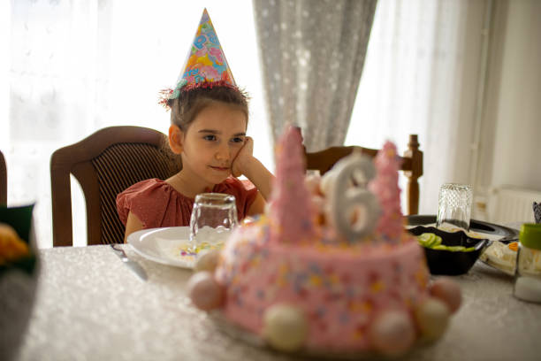 Lonely girl in party hat celebrating birthday alone.