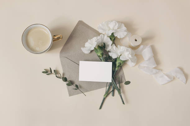 composición femenina del desayuno. maqueta de tarjeta de visita. papelería de boda o cumpleaños. taza de café, flores de claveles blancos y ramas de eucalipto. fondo de mesa beige. plano, vista superior. - food and drink holidays and celebrations isolated objects birthdays fotografías e imágenes de stock