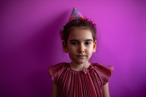 Cute little girl with party hat isolated on purple background