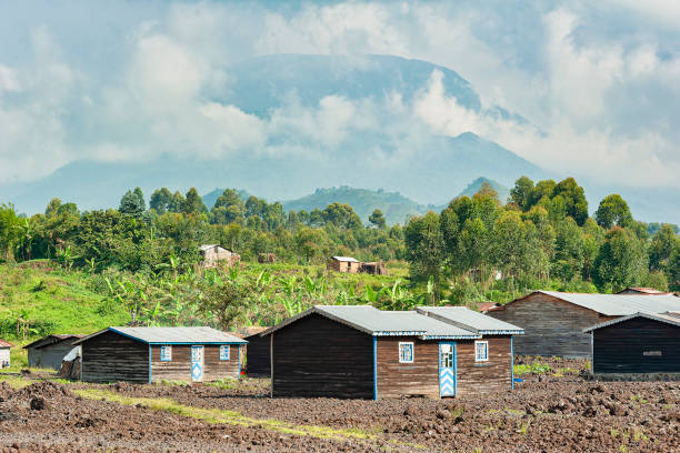 Newly built homes in the lava flow of Nyiragongo Volcano, Goma, Congo Goma, Democratic Republic of Congo - March 07, 2020:
Newly built homes in the lava flow of Nyiragongo volcano,  in the background Nyiragongo volcano is visible. 

Goma is the capital of the province of North Kivu in DR Congo, the town lies between the Nyiragongo volcano and Lake Kivu. Large areas of Goma has been destroyed from the Lava Flow after the deadly eruption of Nyiragongo Volcano on January 17th, 2002. Along the way from the crater to the shores of Lake Kivu the lava flow destroyed 45 villages and about 16,000 homes, leaving about 350,000 people homeless. It is estimated that about 14o people died. In the background a new house which was built after the devastation. Mount Nyiragongo is an active Stratovolcano with an elevation of 3470 m (11382 ft) and is located about 20 km north of the town of Goma, close to the border to Rwanda lake kivu stock pictures, royalty-free photos & images