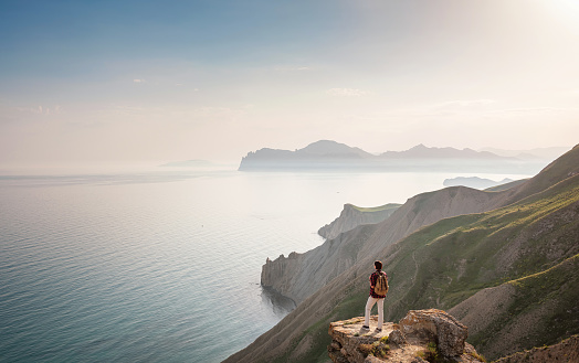 A young Asian woman with a backpack hiking in the summer. Mountain and coastal travel, freedom and an active lifestyle. Breathtaking scenery of the Black Sea coast