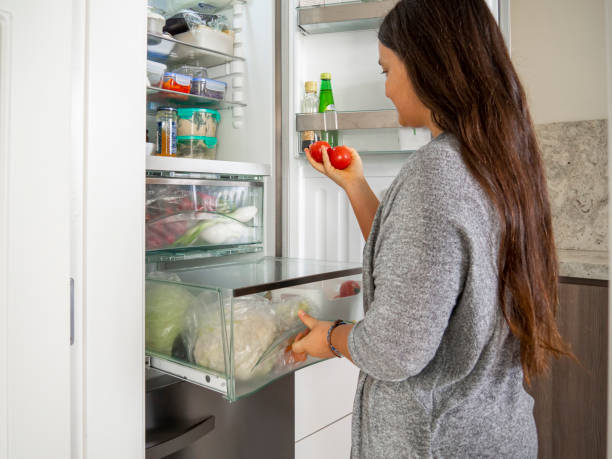 istock Woman with two tomatoes with open drawer in the fridge. 1319743365