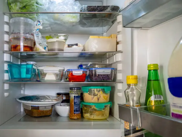 Open fridge with food leftovers and meal plan in glass containers. Domestic refrigerator for healthy eating. Leftover food, yogurt, cheese and other groceries.