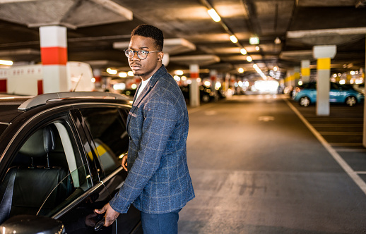 Serious African American entrepreneur getting in his car at public car garage.