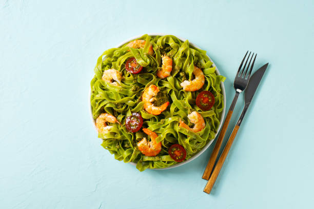 istock Green pasta with shrimp, basil and tomato on blue background, top view, copy space, flat lay 1319744523