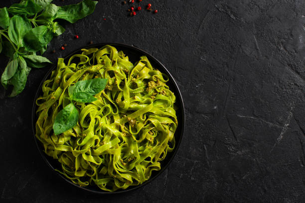 istock Green vegetarian basil pasta with pesto on black background 1319744537