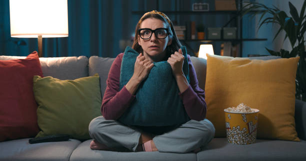 Woman watching a horror movie at home Frightened woman sitting on the couch and watching a horror movie on TV, she is hugging a pillow features stock pictures, royalty-free photos & images