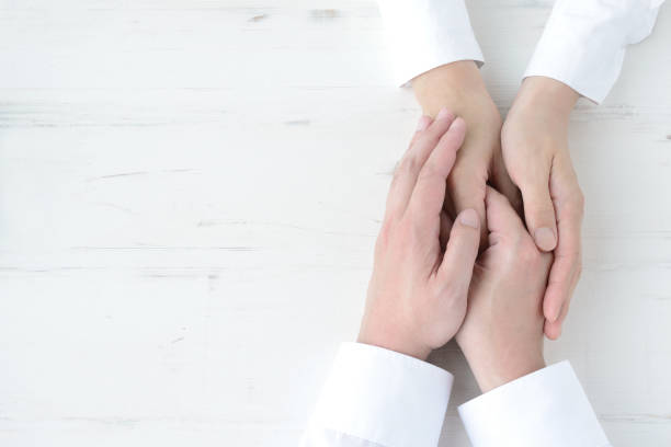 istock Cople's hands held each other on natural white wooden board 1319744848