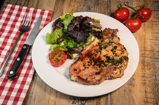 Recipe for grilled pork chop, maple syrup and fresh cilantro marinade, parsley, garlic, served with a salad. High quality photo