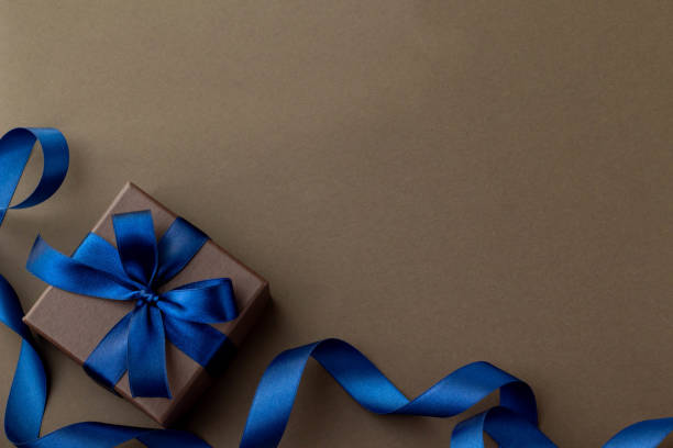 Image of gift with bright blue ribbon and dark brown background stock photo