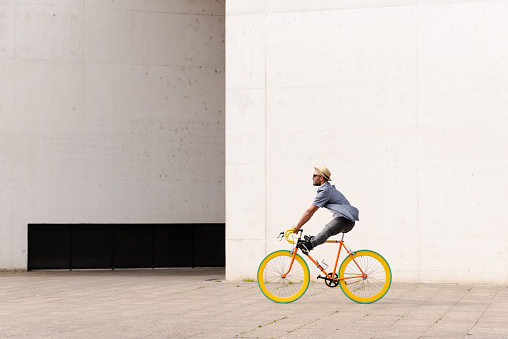 Happy hispanic man riding a vintage colorful bicycle. Urban ecologic transport and sustainable city concept. Copy space on white wall.