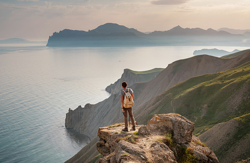 Young man travels alone on the backdrop of the mountains enjoy view of beautiful landscape natural mountain with sea, the lifestyle concept of traveling outdoors.