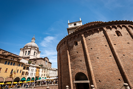 Mantua downtown, Church Rotonda di San Lorenzo in Romanesque style (1083-XI century) and the Basilica and Cathedral of Sant’Andrea (Saint Andrew, 1472-1732), Piazza delle Erbe (Square of Herbs), Lombardy, Italy, southern Europe.The ancient square is crowded with tourists and locals on a sunny spring day.