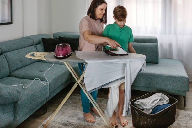 mother teaching her teen son to iron - iron women ironing board stereotypical housewife imagens e fotografias de stock