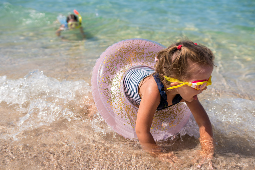 Joyful girl playing on the beach with pink swimming ring. Children having fun by the sea in summertime. Wonderful family getaways. Vacation with kids concept