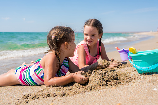 Summer time concept. Two adorable girls having fun on the beach. Children playing with sand. Family vacation at sea with kids