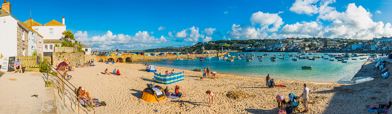 Crowds of holiday makers, day trippers and tourists enjoying the summer sunshine on the popular harbour beach of St. Ives, Cornwall.