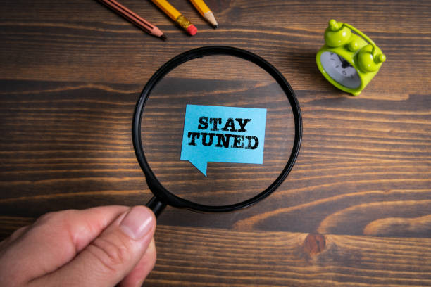 istock Stay Tuned. Speech bubble and green alarm clock on a wooden background 1319762408