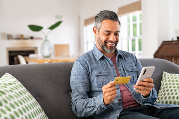 Mixed race man paying online on mobile phone Middle eastern mature man with beard using credit card to make online payment on smartphone. Mixed race man holding debit card and using cellphone for shopping online from home. Smiling indian guy using smart phone to check credit card transactions from app. paid stock pictures, royalty-free photos & images