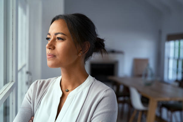 Thoughtful black woman looking outside window Mature african woman looking outside window with uncertainty. Thoughtful mid adult woman looking away through the window while thinking about her future business after pandemic. Close up face of doubtful lady at home with pensive expression and copy space. west asian ethnicity photos stock pictures, royalty-free photos & images