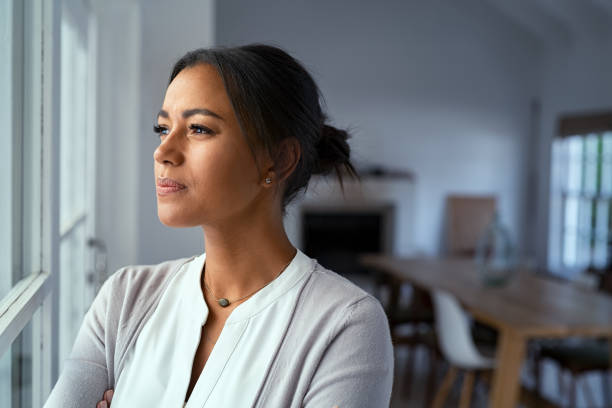 Thoughtful black woman looking outside window Mature african woman looking outside window with uncertainty. Thoughtful mid adult woman looking away through the window while thinking about her future business after pandemic. Close up face of doubtful lady at home with pensive expression and copy space. thinks stock pictures, royalty-free photos & images