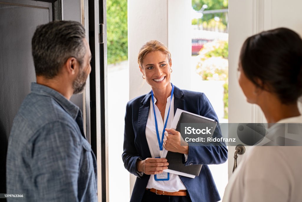 Social counselor meeting couple at home Smiling mature social counselor meeting mature couple at home. Happy multiethnic man and latin woman greeting agent at home standing near door. Successful social worker consultant on the doorstep meeting ethnic couple. Real Estate Agent Stock Photo
