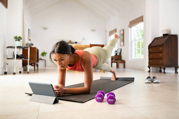 mieszana kobieta wyścigu robi deskę i oglądanie lekcji online - stretching yoga exercise mat women zdjęcia i obrazy z banku zdjęć